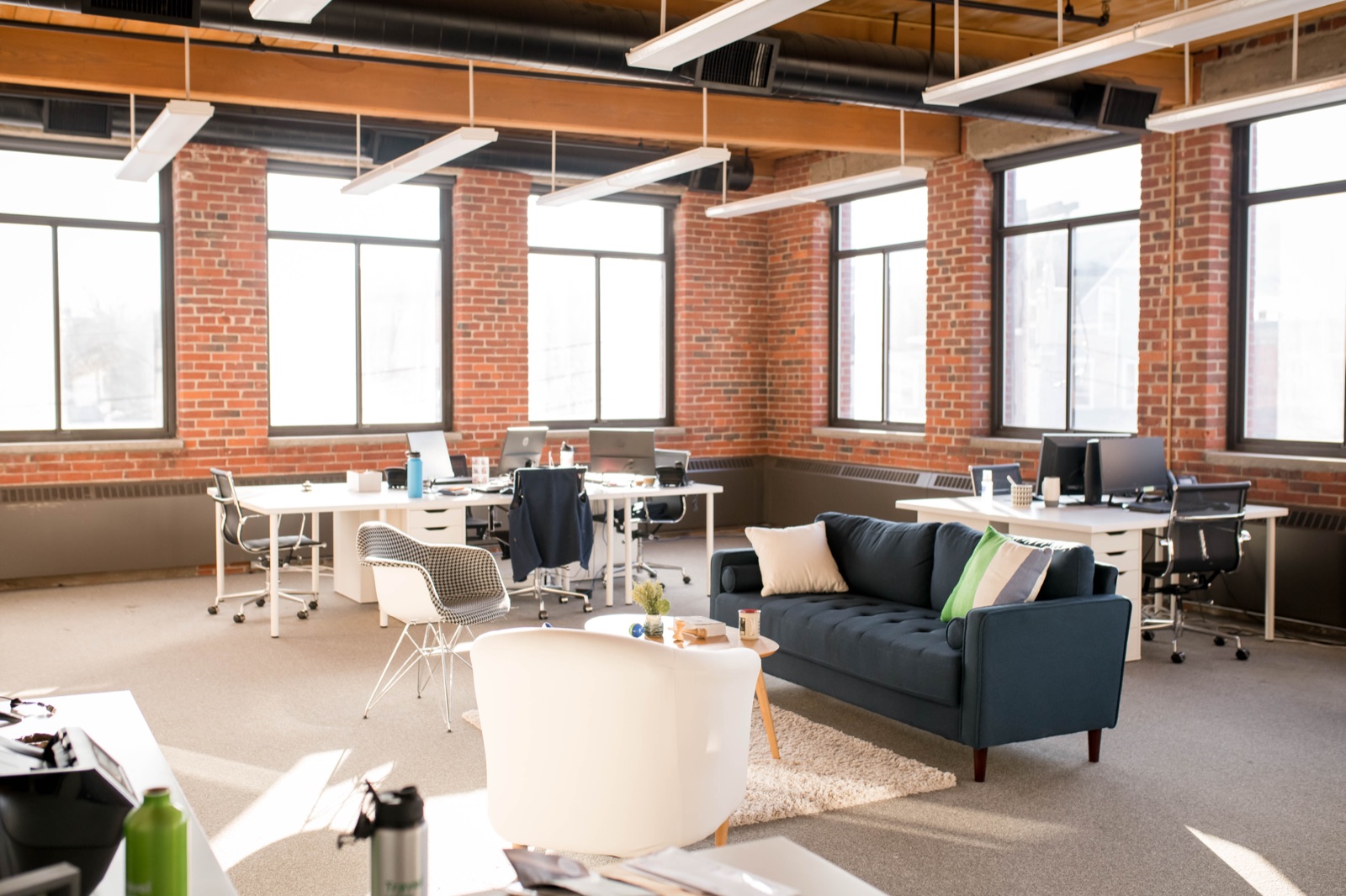 Sunlit corner suite with exposed brick, workstations, and a lounge corner